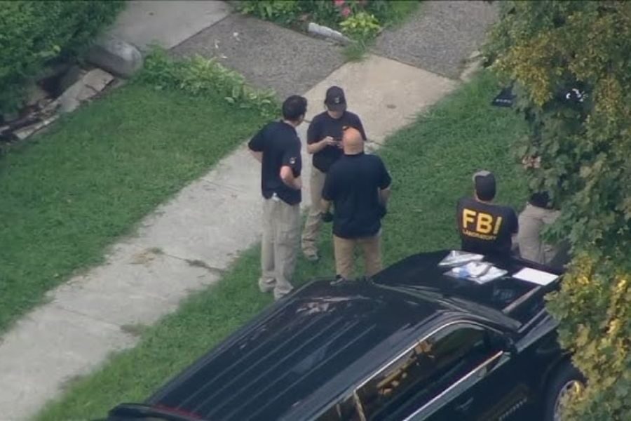 Aerial view of FBI agents and law enforcement officials gathered outside a residence near a black SUV.
