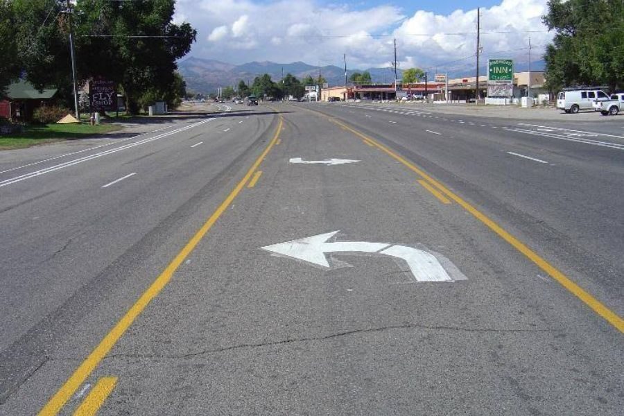 Wide road with multiple lanes and white painted arrows indicating left and U-turn directions.