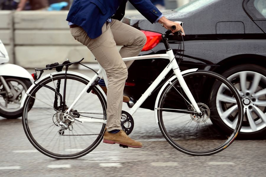 Man in business attire riding a white bicycle in urban traffic next to a black car.