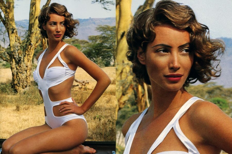 A model in a white cutout swimsuit poses in the savanna with curled vintage-inspired hair and confident expression.