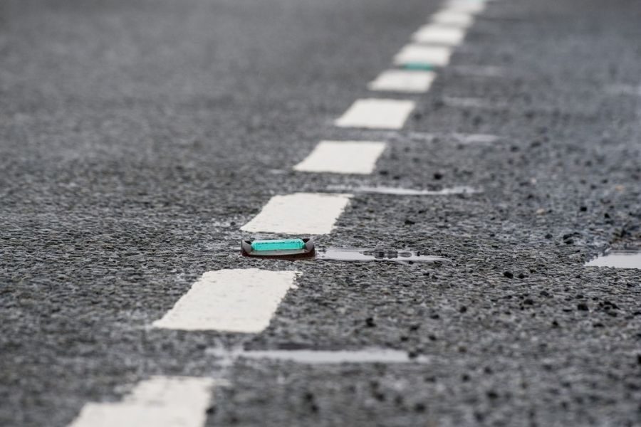 Close-up of reflective road studs and white dashed lane markings on wet asphalt.