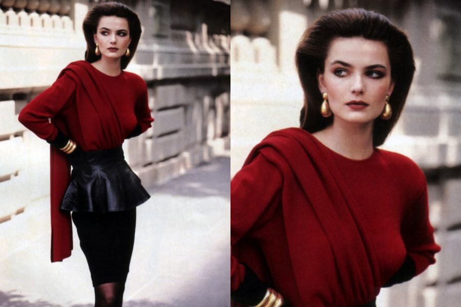 A model wears a red draped top and black pencil skirt with gold earrings, posing with hands on hips in an urban setting.