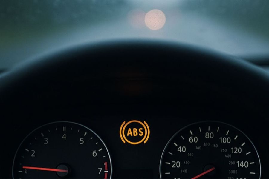 Car dashboard showing illuminated ABS warning light between speedometer and tachometer.
