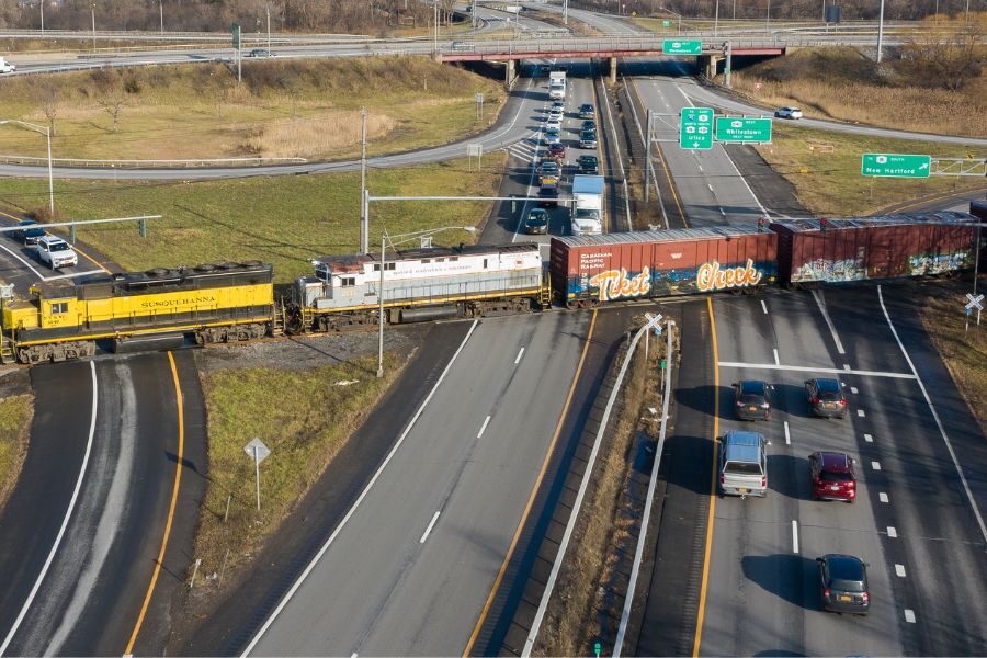 Freight train blocking traffic on a major divided highway near multiple freeway entrance ramps.