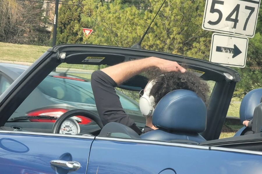Person wearing large white headphones while driving a blue convertible with the top down, passing a road sign for Route 547.
