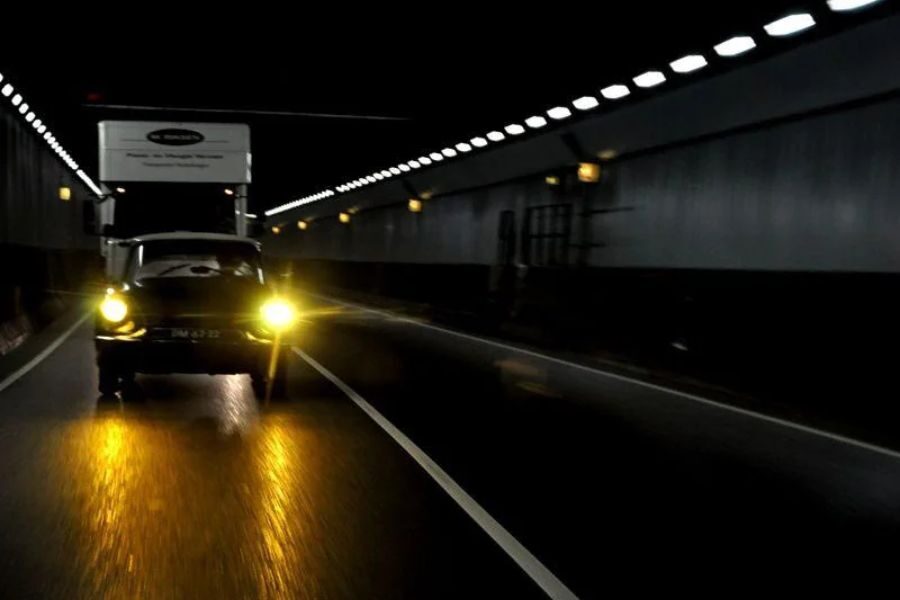 Car with yellow headlights driving through a dark tunnel with a truck closely following behind.