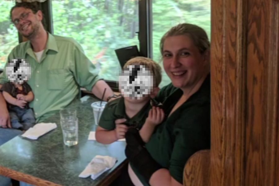 A family sits together in a booth on a train with wooded scenery visible through the window. The parents smile while children with pixelated faces sit on their laps.
