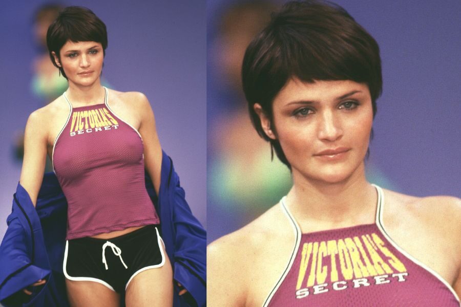 A model with a short pixie cut walks the runway in a sporty purple halter top and black athletic shorts that say “Victoria’s Secret.”