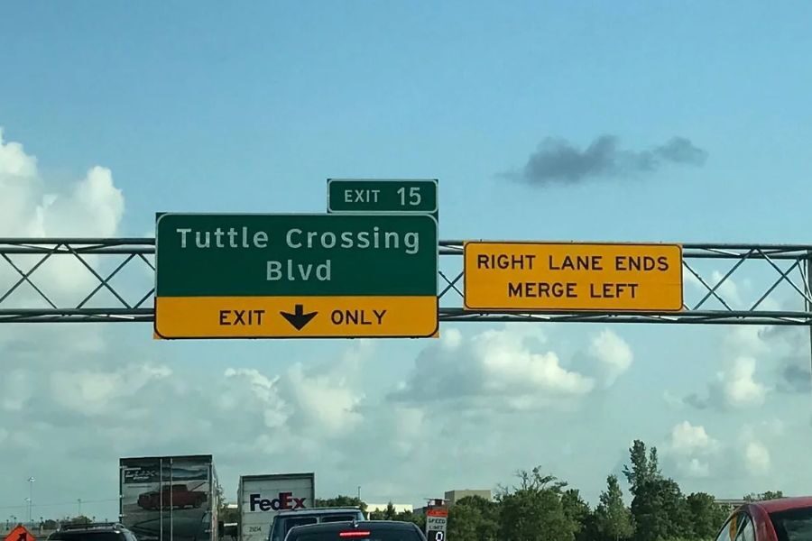 Overhead highway signs showing Tuttle Crossing Blvd exit and a warning that the right lane ends and traffic must merge left.