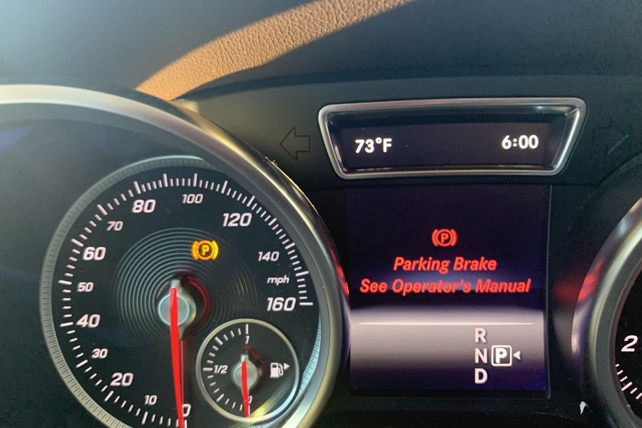 Car dashboard display showing a parking brake warning light and message to consult the operator’s manual.