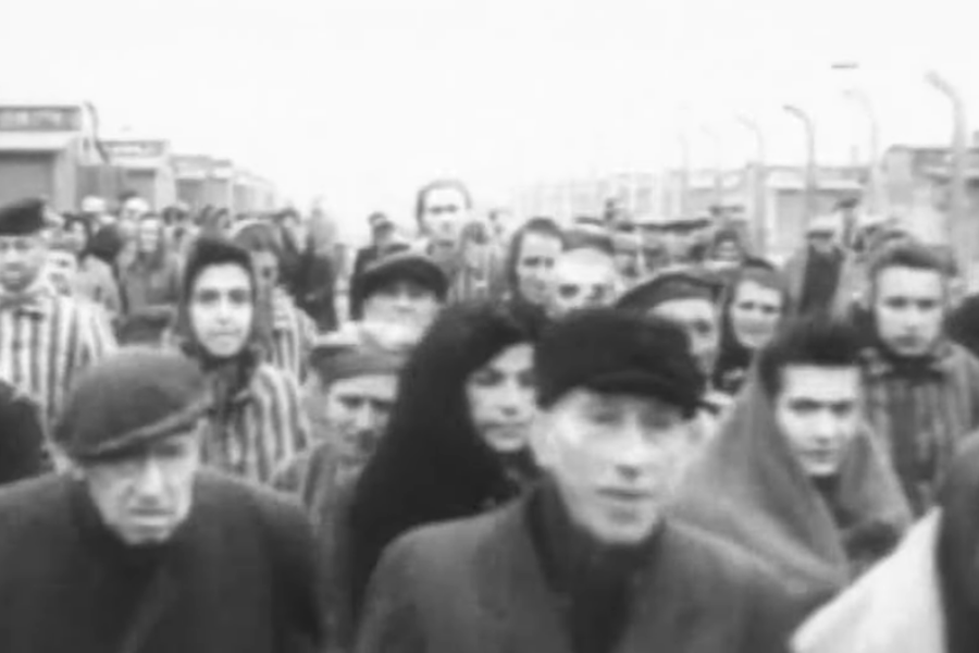 Black and white photo showing Holocaust survivors in striped uniforms and civilian clothes walking in a crowd after liberation from a concentration camp.