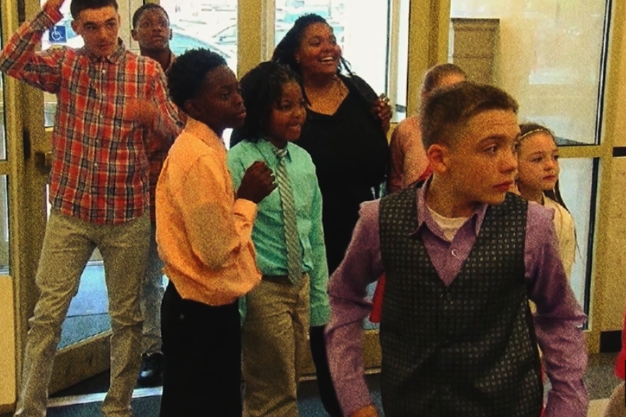 A group of children and a woman gathered near glass doors, appearing to be entering or exiting a building.