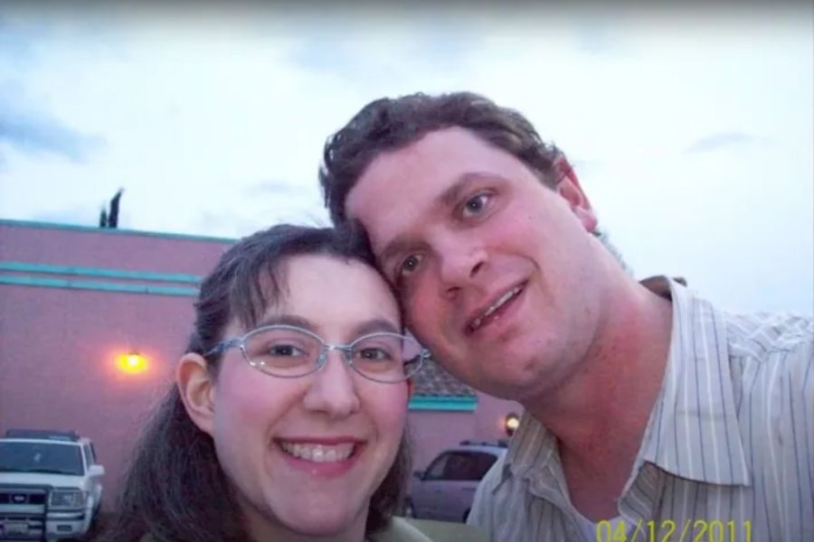 A smiling couple takes a close-up selfie outside a building with pink walls and teal trim at dusk. The date in the corner reads 04/12/2011.
