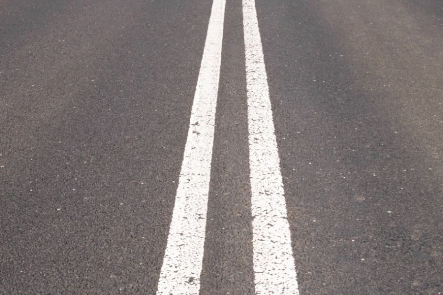 Two solid white lines painted on asphalt, indicating a no-passing zone on a roadway.