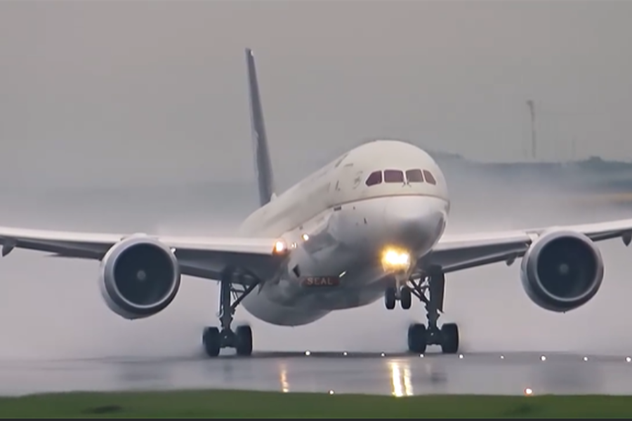 A commercial airplane touches down on a wet runway with landing lights on, creating mist behind its wheels.