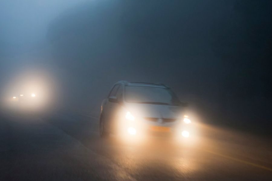 Cars driving through dense fog with headlights on, reducing visibility significantly on the road.