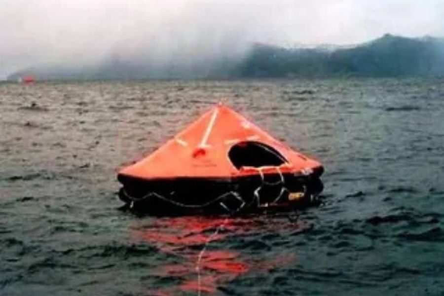 Bright orange life raft floating on dark, choppy waters under a cloudy, overcast sky. The scene evokes a sense of isolation and urgency.