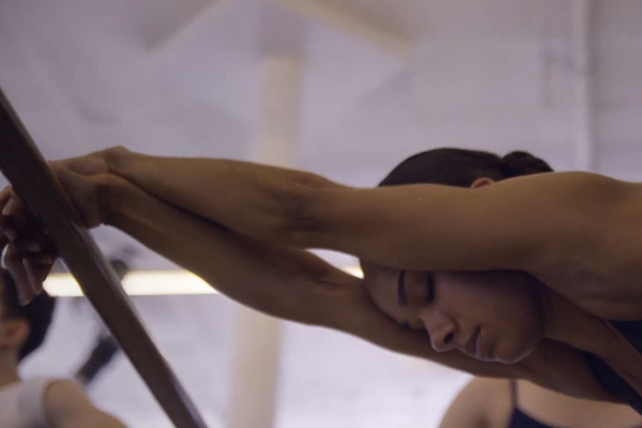 A dancer leans forward with eyes closed, arms outstretched on a ballet barre. The serene studio atmosphere conveys focus and tranquility.