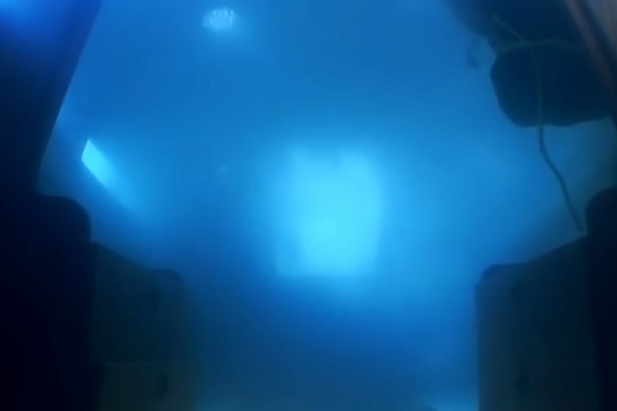 Underwater scene with a deep blue hue, light filtering through water. Submerged objects faintly visible, creating a mysterious, tranquil atmosphere.