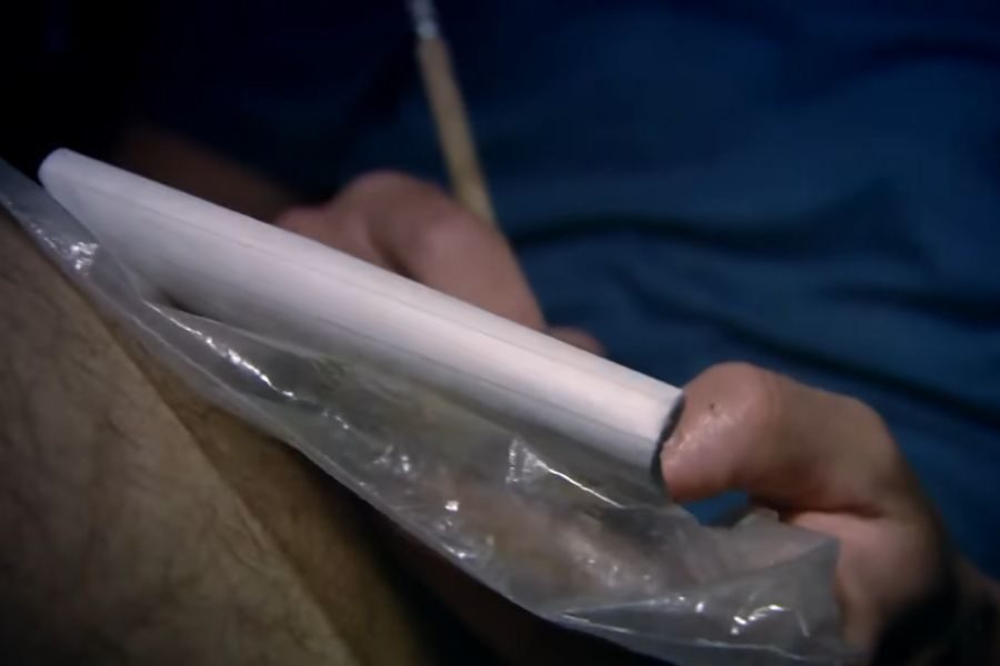 A close-up of a hand holding a smartphone wrapped in a plastic bag. The background is blurred, suggesting a protective or makeshift use, with a casual tone.