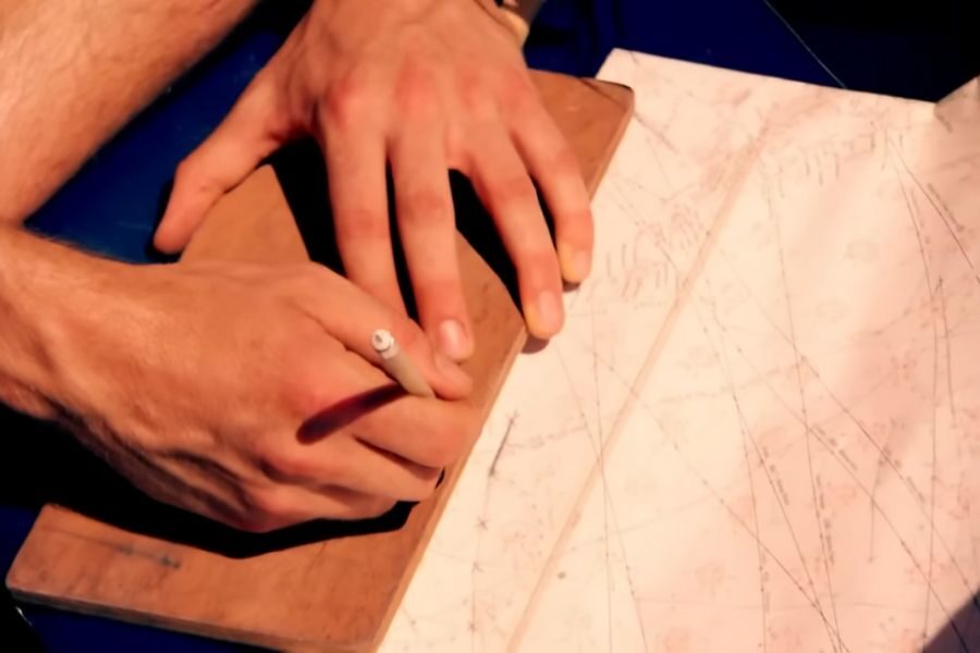 Hands using a pencil to write on a wooden slab next to a detailed, lined map. The scene conveys focus and determination.
