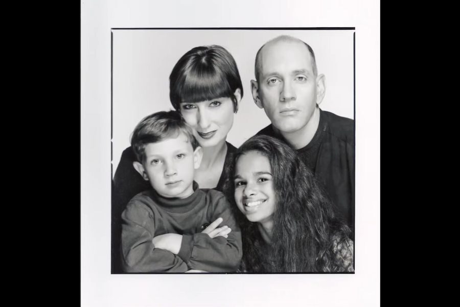 Black and white portrait of a family with two adults and two children. The adults stand behind the children, who are smiling, conveying warmth.